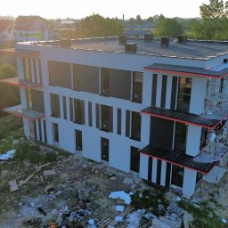 DEVELOPMENT SP Z O O - Wysoki, nowoczesny budynek wielorodzinny w trakcie budowy, z widocznymi rusztowaniami i elementami wykończeniowymi. Ujęcie z góry, w tle zieleń i zabudowa jednorodzinna.