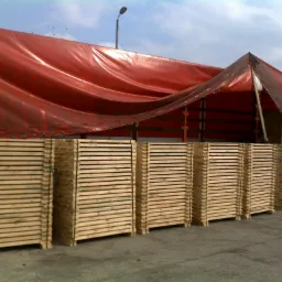 Stosy drewnianych palet Euro/Epal ułożone przed naczepą ciężarówki z czerwoną plandeką, widok z boku.