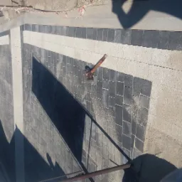 Świeżo ułożona, dwukolorowa kostka brukowa z gumowym młotkiem leżącym na powierzchni; widoczne samochody i otoczenie.