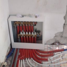 KANMAKS - Rozdzielacz ogrzewania podłogowego z czerwonymi i białymi rurami w szafce, instalacja w trakcie montażu, widoczny styropian z rastrem pod rury.