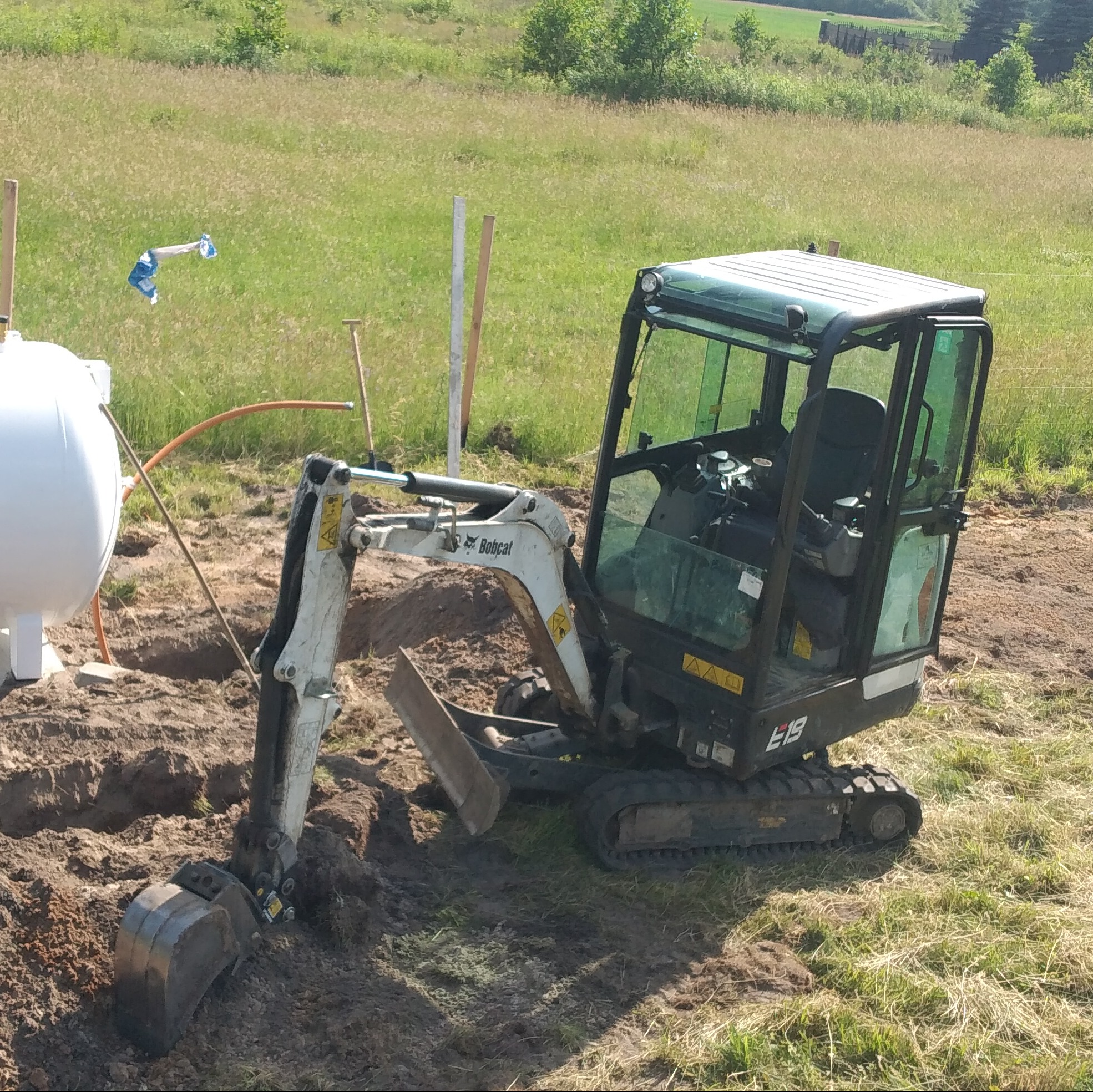 Mini koparka Bobcat E19 w trakcie prac ziemnych przy zbiorniku, prawdopodobnie podczas instalacji w gruncie.