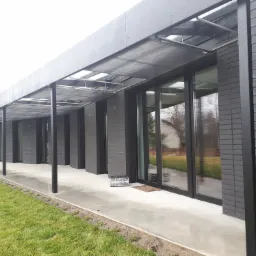 Nowoczesny dom z dużymi oknami w czarnych ramach i zadaszeniem w Tarnowskich Górach, widok z zewnątrz, zieleń trawnika.