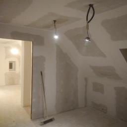 P.P.U.H Wojkoz - Pokój na poddaszu w trakcie szpachlowania i przygotowania ścian, widoczne łączenia płyt gipsowo-kartonowych, tymczasowe oświetlenie i narzędzia.