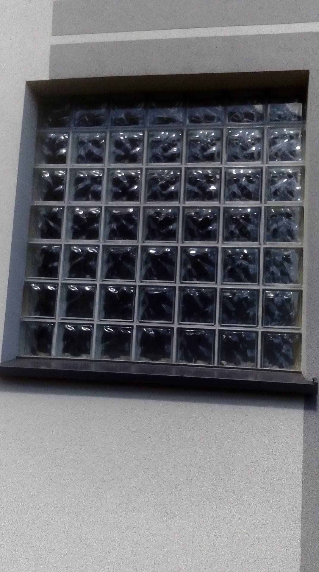 Ściana z wbudowanym oknem z luksferów, widoczne z bliska, z delikatnym oświetleniem.