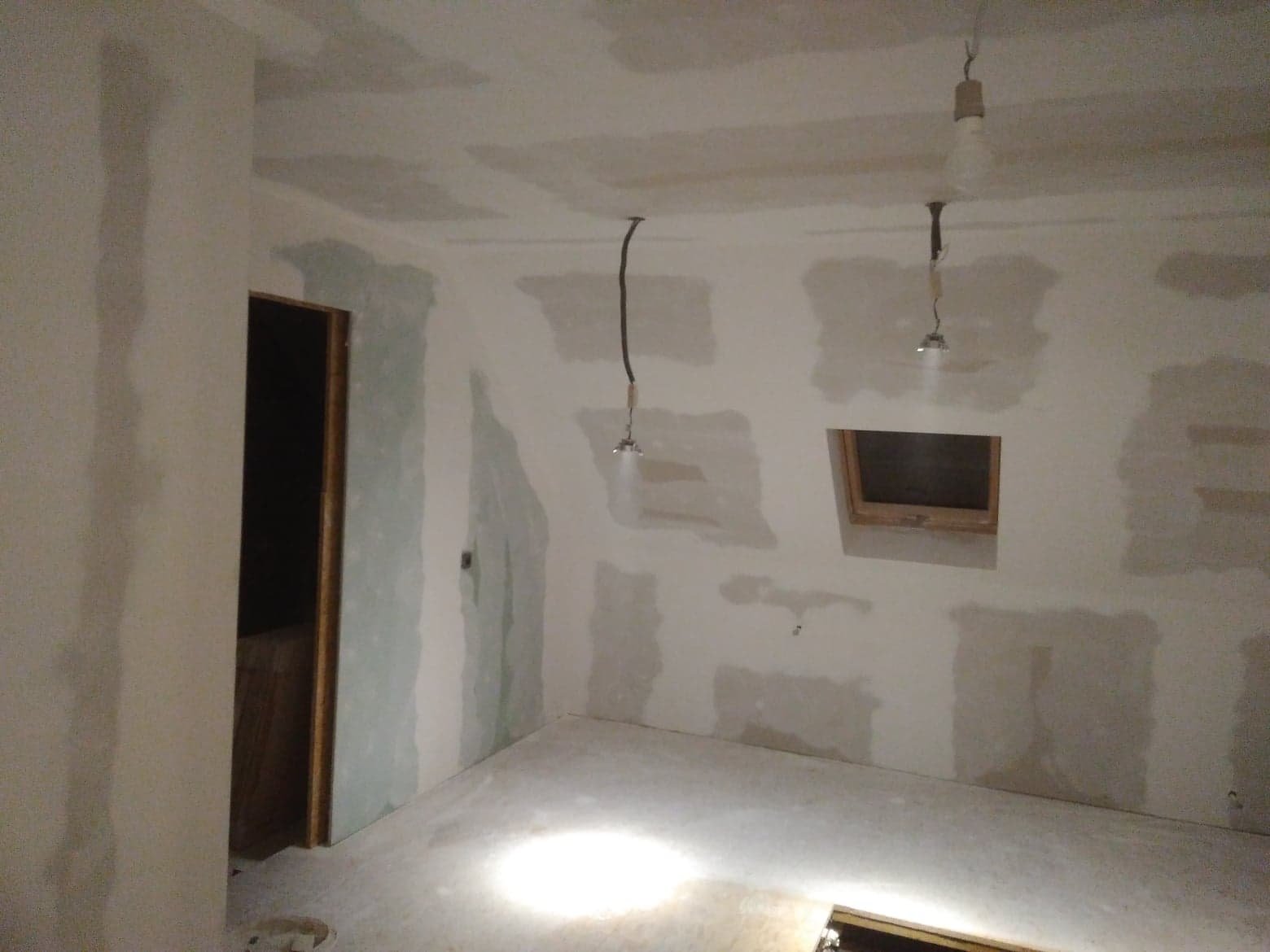 Pokój na poddaszu w trakcie wykańczania: płyty karton-gips na ścianach i suficie, widoczne łączenia wymagające szpachlowania, surowe oświetlenie tymczasowe, okno dachowe.