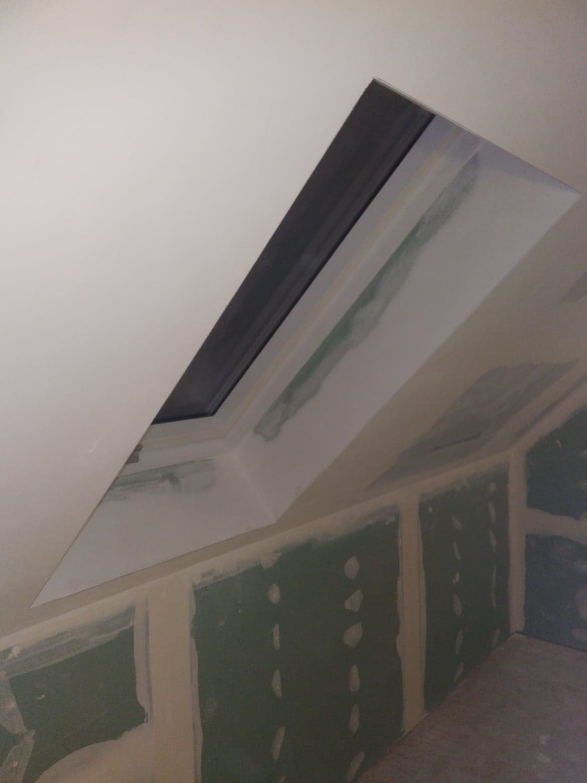 Montaż okna dachowego w skośnej ścianie z płyt kartonowo-gipsowych, widoczne szpachlowanie łączeń.