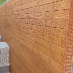 Ukończony taras z desek kompozytowych w odcieniach brązu, przylegający do ściany budynku wykończonej kamieniem dekoracyjnym, z widoczną kostką brukową w tle.