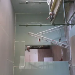 Wnętrze w trakcie montażu płyt kartonowo-gipsowych, widoczne rusztowanie i otwór drzwiowy do innego pomieszczenia.