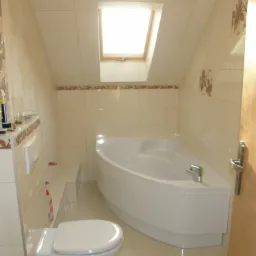 Jasna łazienka na poddaszu w Ostrożnicy z narożną wanną, beżowymi płytkami z motywem kwiatowym i oknem dachowym.