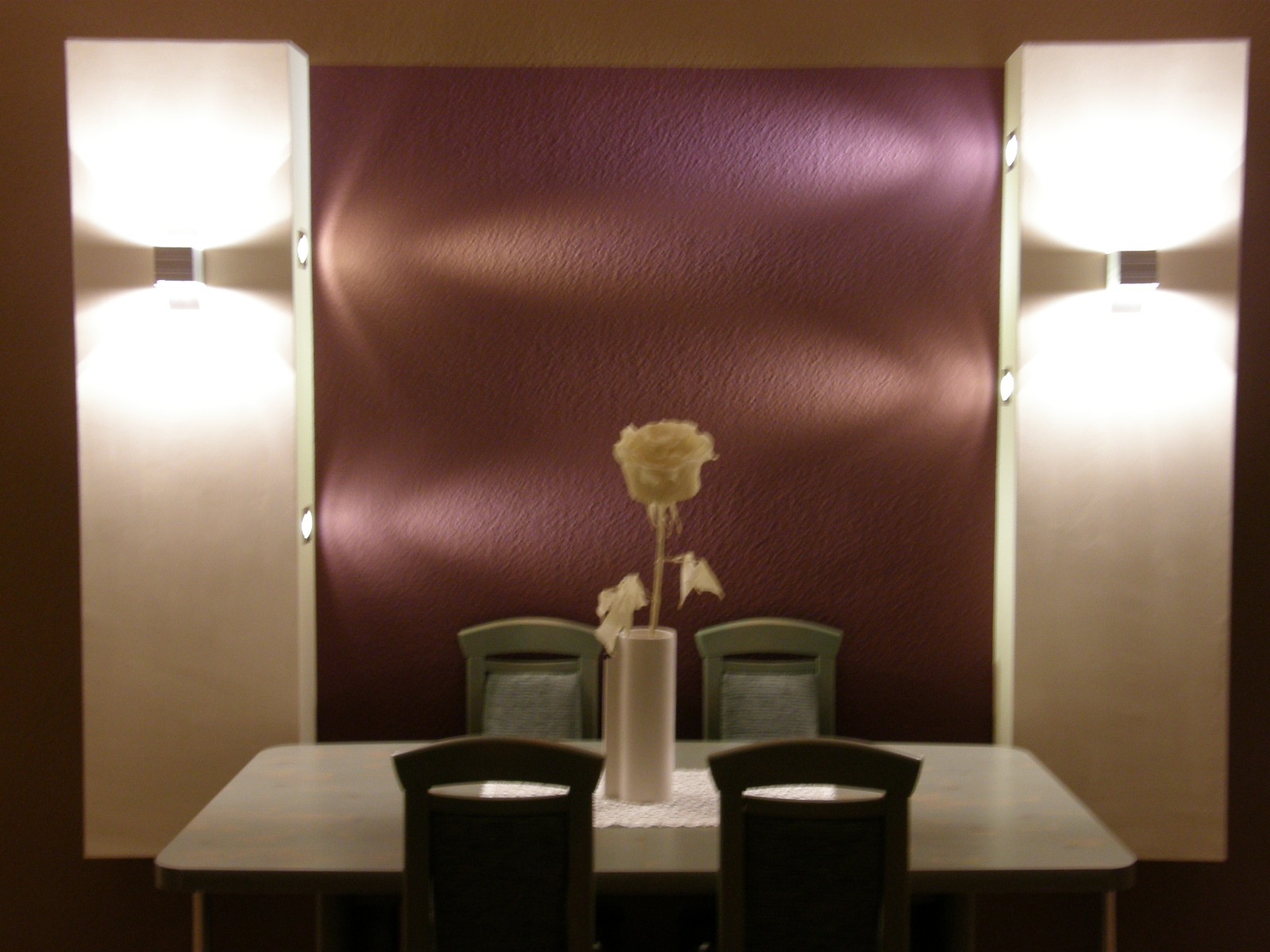 Jadalnia z fioletową ścianą, oświetleniem punktowym i kwiatem w wazonie na stole, widok z przodu na cztery krzesła.