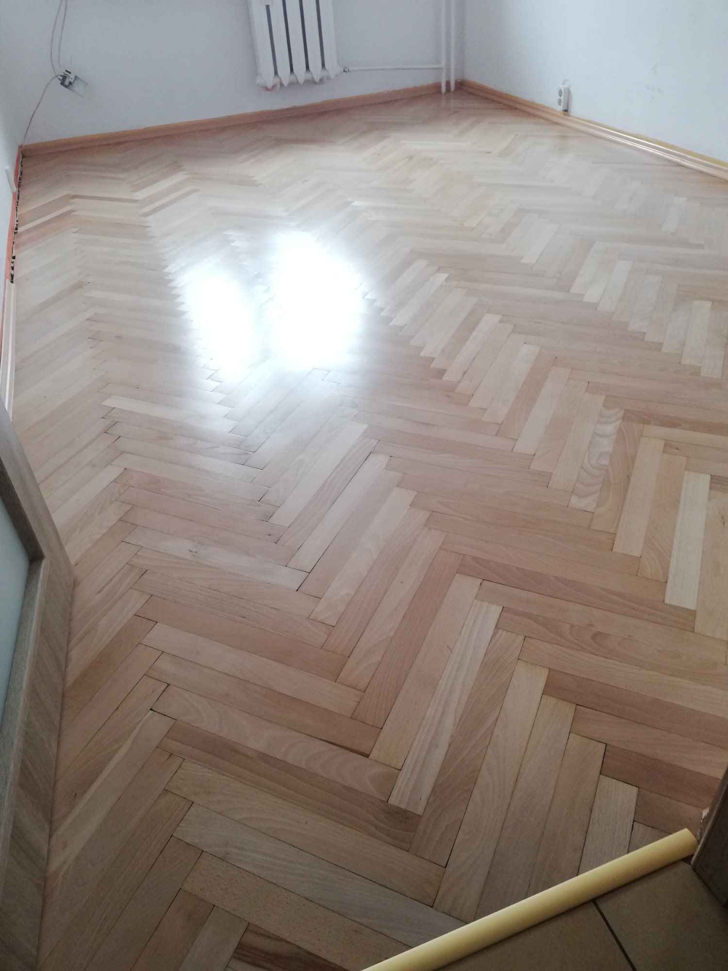 Jasna, odnowiona podłoga parkietowa ułożona we wzór jodełki, widoczne listwy przypodłogowe i kaloryfer w rogu pomieszczenia.