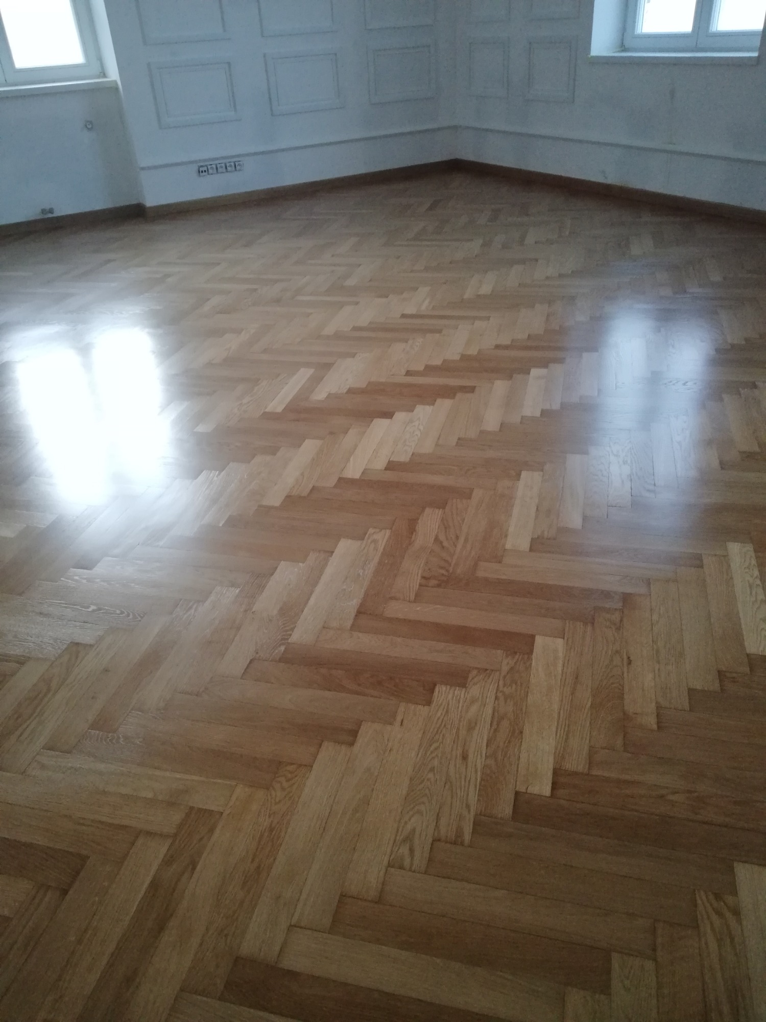 Parkiet ułożony w jodełkę po renowacji, widoczne odbicie światła okiennego na gładkiej powierzchni.