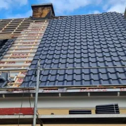 Częściowo pokryty dach z czarnej dachówki, widoczne rusztowania i niezakończona część konstrukcji dachu z membraną i łatami, komin w tle.