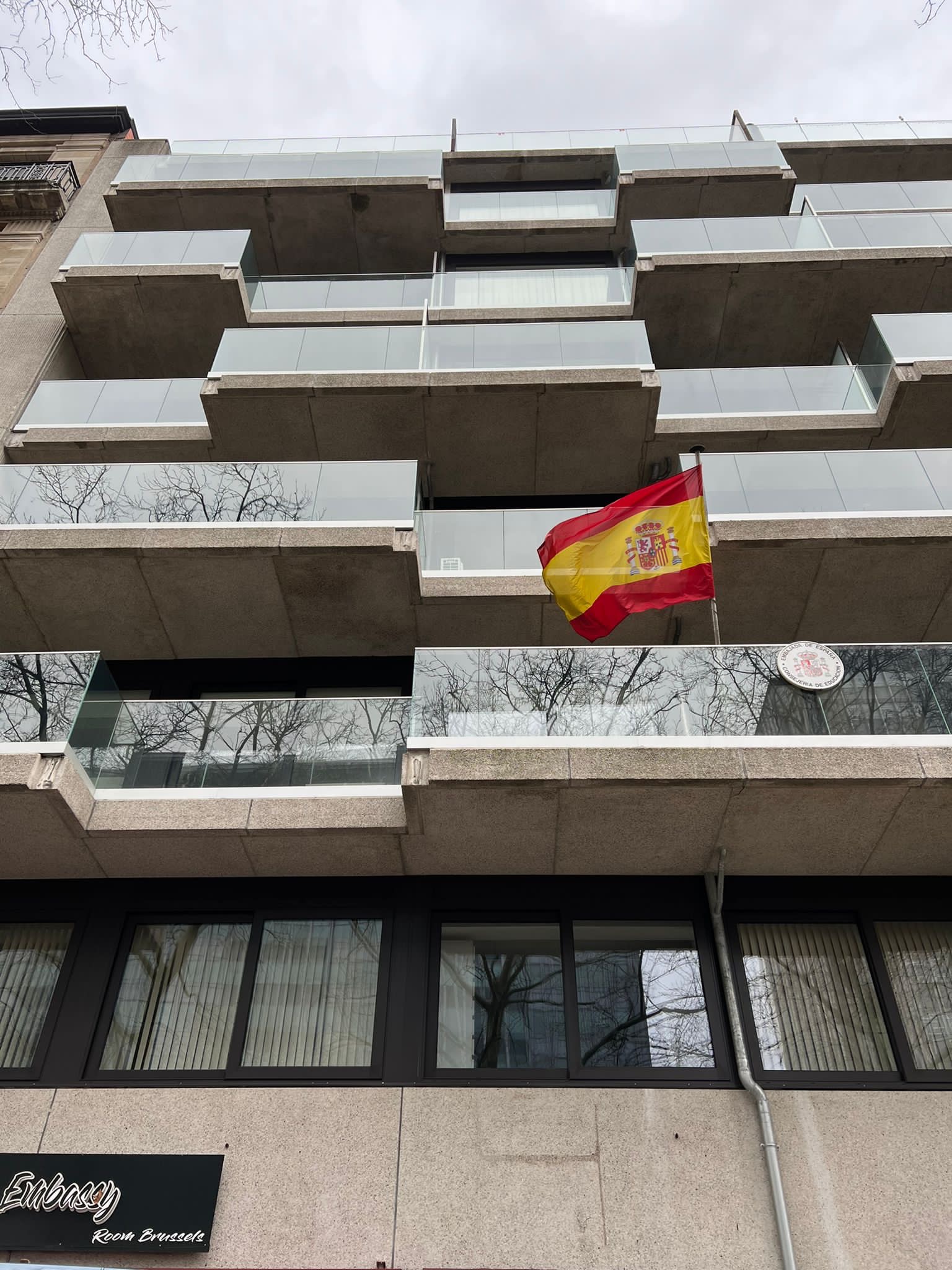 Budynek z balkonami zabezpieczonymi szklanymi balustradami, na jednym z balkonów powiewa flaga Hiszpanii
