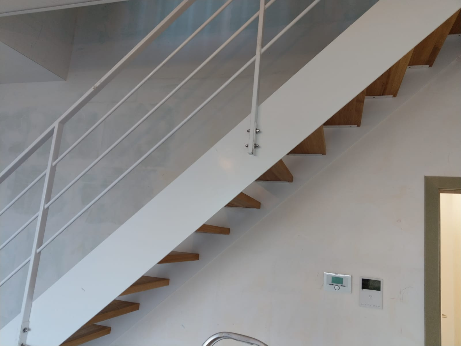 Nowoczesne schody z drewnianymi stopniami i białą konstrukcją stalową, zabezpieczone metalową balustradą z poziomymi prętami, zamocowaną za pomocą śrub.