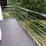 Balkon z nowoczesną balustradą ze stali nierdzewnej, poziome pręty, szara płytka podłogowa, widok na zieleń w tle.