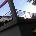 Nowoczesna balustrada szklana z elementami metalowymi, zamontowana na tarasie, widok z dołu na błękitne niebo.