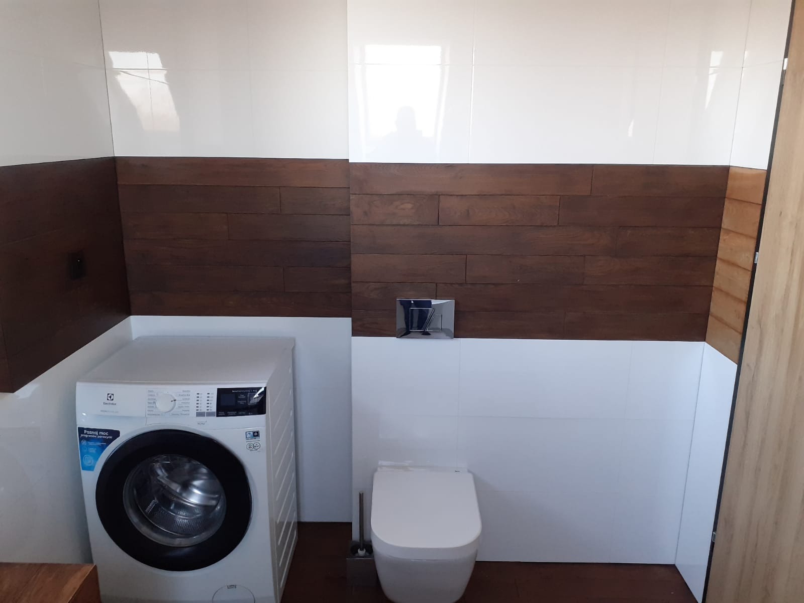 Nowoczesna łazienka z białymi płytkami, drewnianą boazerią, podwieszaną toaletą i pralką Electrolux