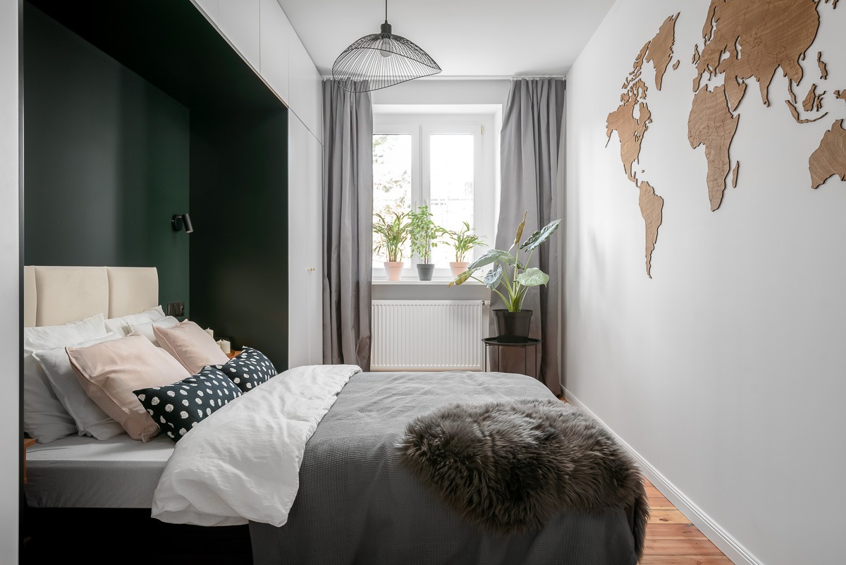 Nowoczesna sypialnia z łóżkiem, drewnianą mapą świata na ścianie, roślinami w oknie i lampą wiszącą z metalowego drutu.