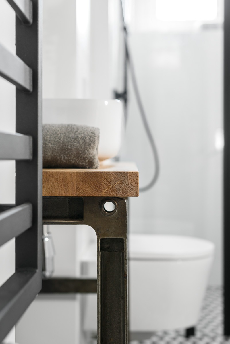 Nowoczesna łazienka w Zielonej Górze z umywalką nablatową, drewnianym blatem i metalową konstrukcją, widoczny grzejnik drabinkowy i fragment kabiny prysznicowej.