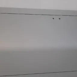 Szara, zamknięta szafka wnękowa z dwoma chromowanymi zatrzaskami, umieszczona w białej ścianie.