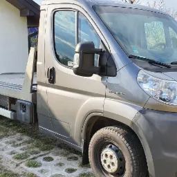 Szara laweta Peugeot zaparkowana na posesji z kostki brukowej i trawy, widoczna brama garażowa w tle.