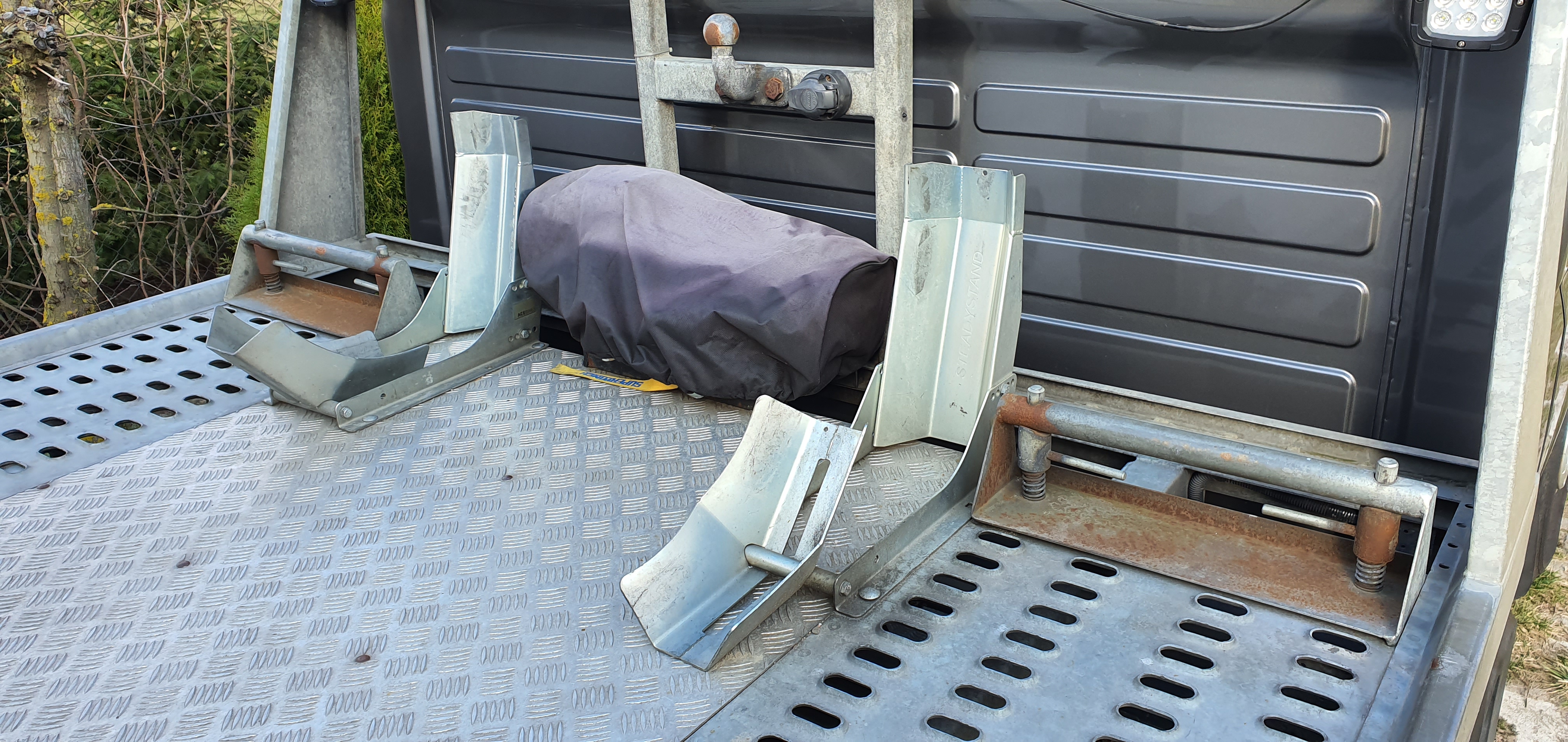 Pusta platforma lawety z zamontowanymi uchwytami na motocykl, jeden z nich przykryty czarnym pokrowcem, widoczna żółta taśma mocująca.