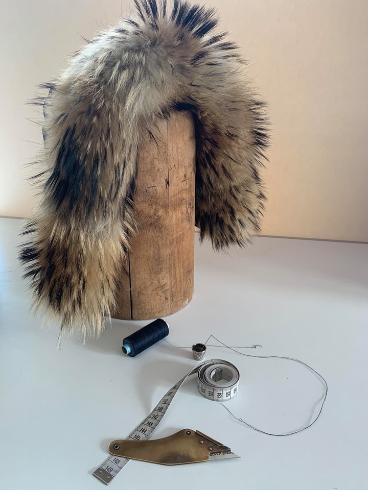 Wykończenie futrzane kołnierza na drewnianym manekinie krawieckim, obok igła, naparstek, nić i miarka krawiecka.