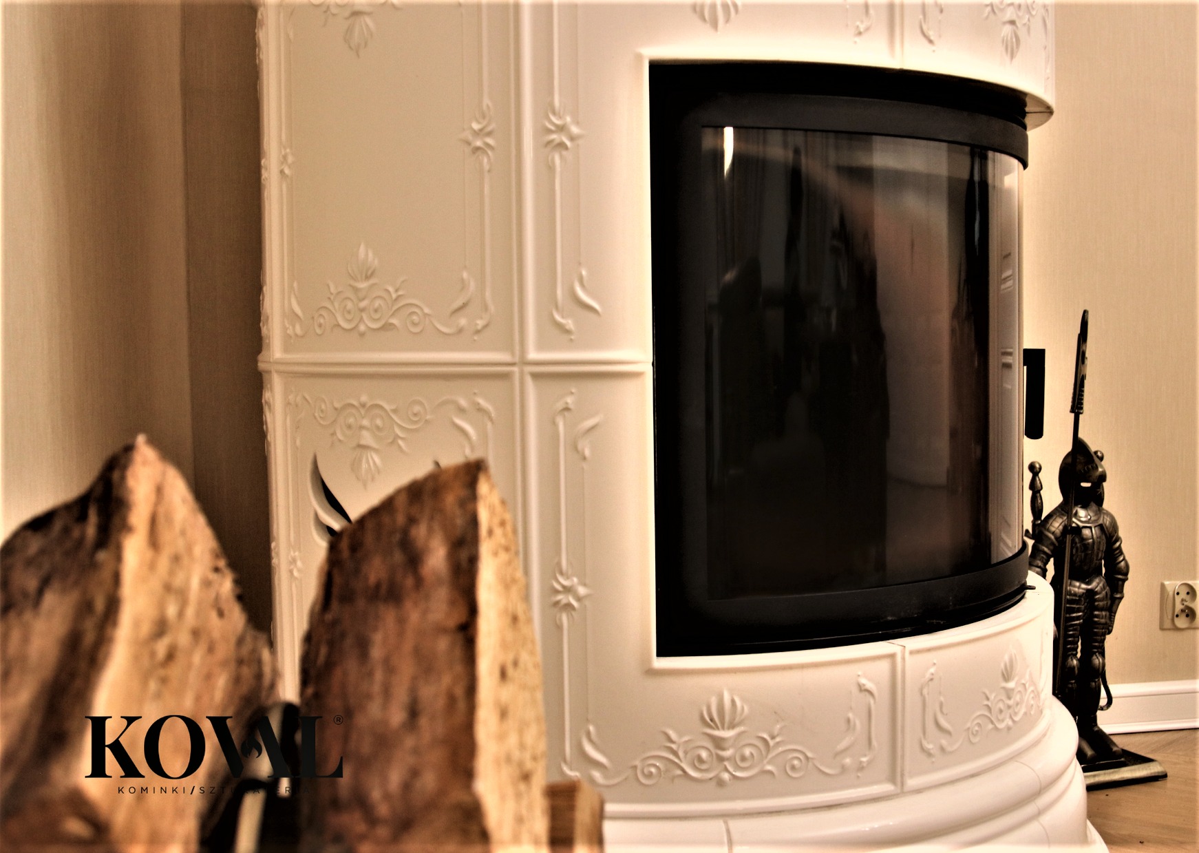Biały, kaflowy kominek z szybą, z dekoracyjnymi zdobieniami. Obok kominka drewno i figurka rycerza. Ciepłe oświetlenie wnętrza.