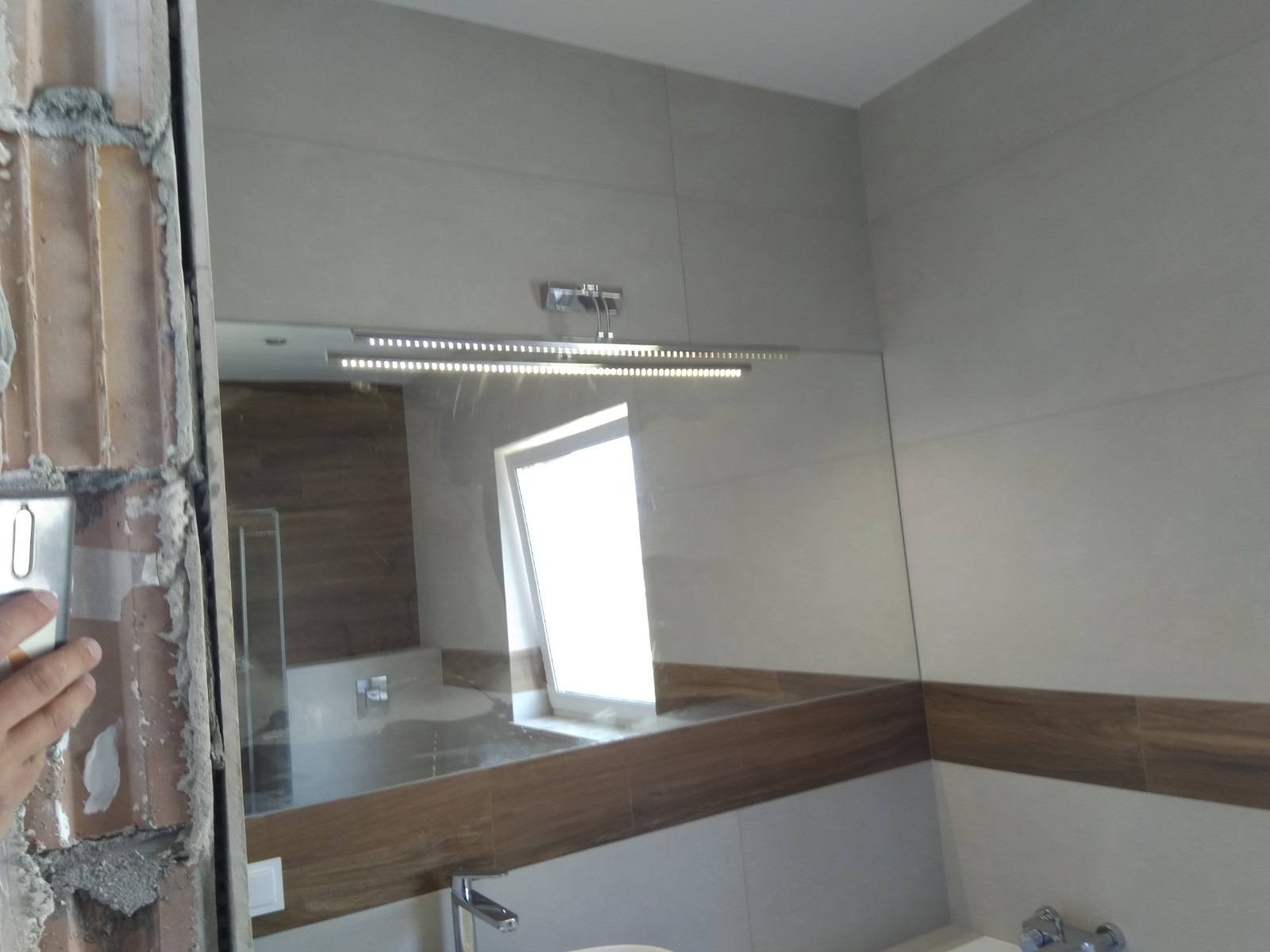 Montaż lustra z oświetleniem LED w łazience w Krakowie, widoczne płytki i fragment ściany w trakcie wykończenia.