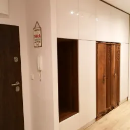 Biała, lakierowana szafa wnękowa z drewnianą wnęką i wkomponowaną szafą w stylu retro, widoczna przy wejściu do mieszkania.