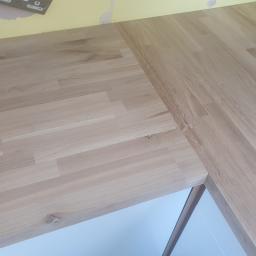 lopezz - Fragment blatu z jasnego drewna klejonego, widoczny na tle żółtej ściany z niedokończonymi pracami malarskimi i białej szafki.