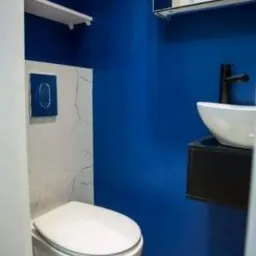 Niebieska łazienka z podwieszaną toaletą, umywalką nablatową i białymi półkami, wykończona marmurową płytką imitującą pęknięcia.