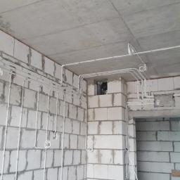 El-Ad - Białe przewody elektryczne poprowadzone po ścianach i suficie z betonu komórkowego w surowym stanie, z widocznymi puszkami instalacyjnymi i otworami w ścianach.