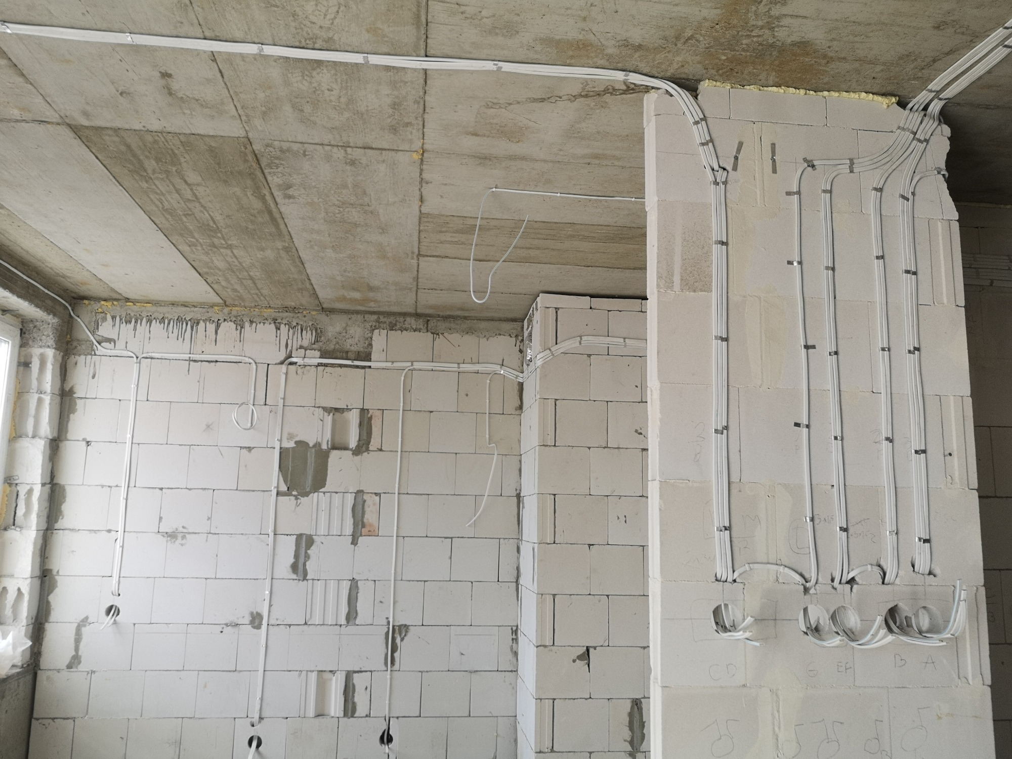 Nowa instalacja elektryczna natynkowa w budynku w stanie surowym, widoczne przewody przymocowane do ścian z betonu komórkowego i sufitu, oznaczenia na ścianie pod przyszłe gniazdka.