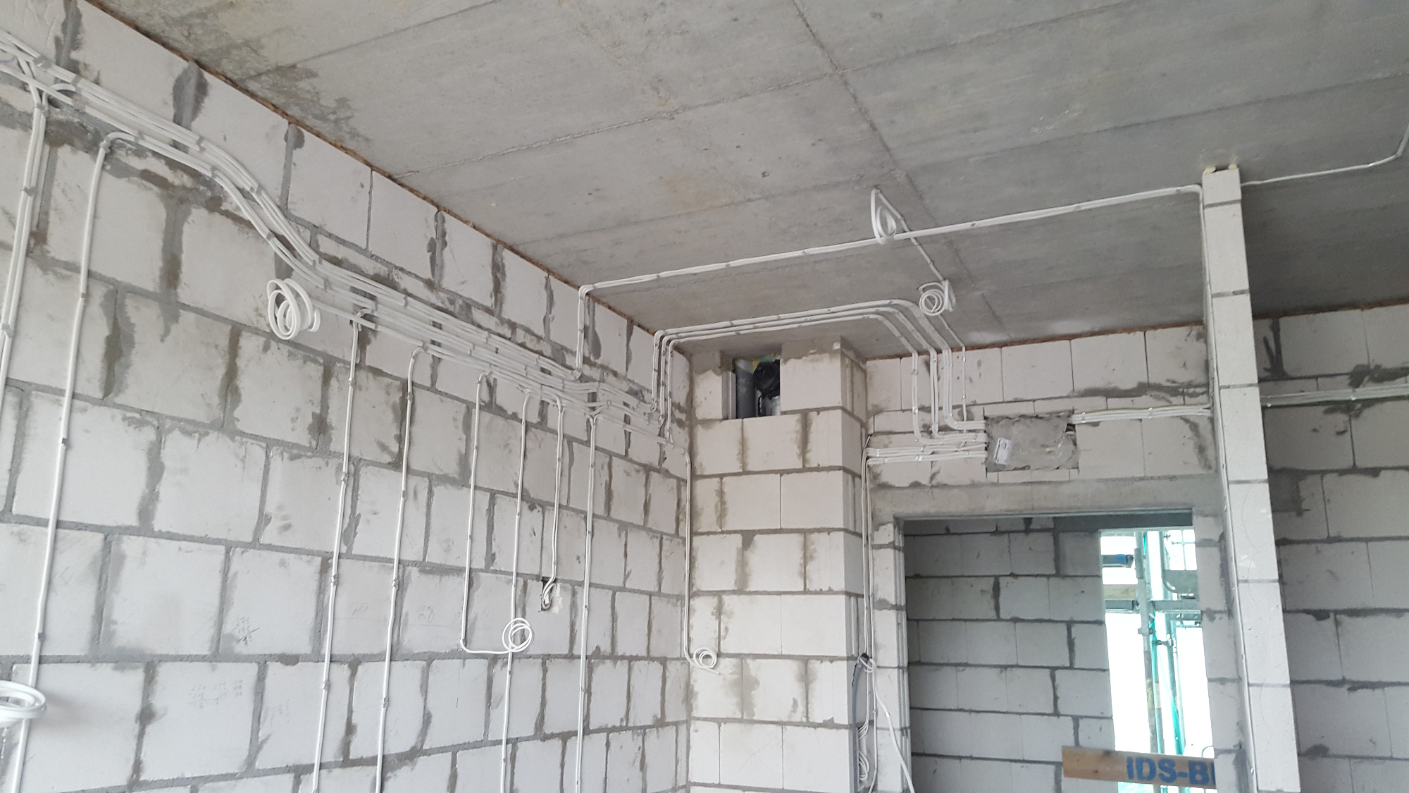 Białe przewody elektryczne poprowadzone po ścianach i suficie z betonu komórkowego w surowym stanie, z widocznymi puszkami instalacyjnymi i otworami w ścianach.