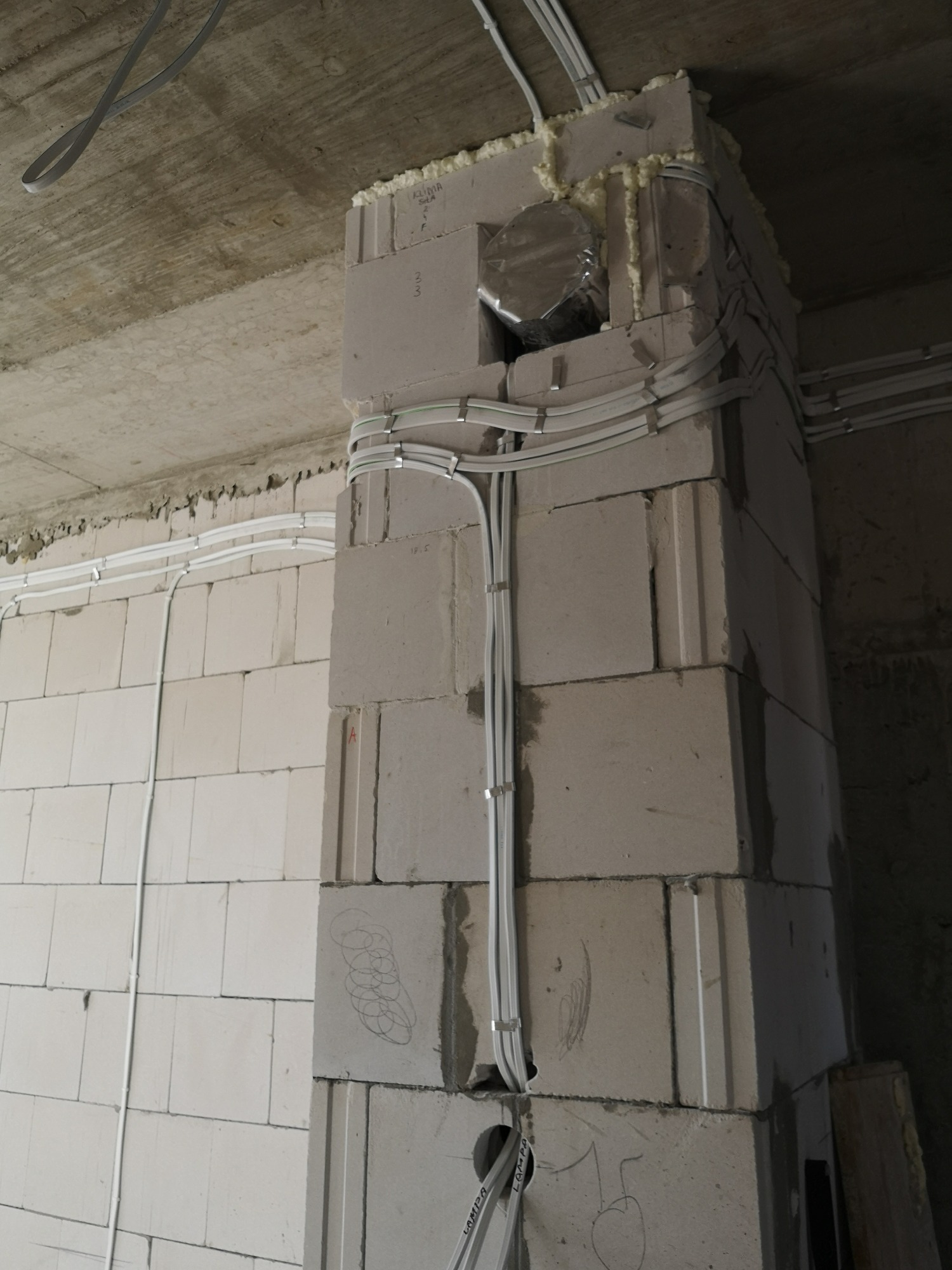 Wewnętrzna instalacja elektryczna w budynku w trakcie budowy, kable przymocowane do ściany z betonu komórkowego za pomocą uchwytów, widoczne oznaczenia ołówkiem na ścianie.