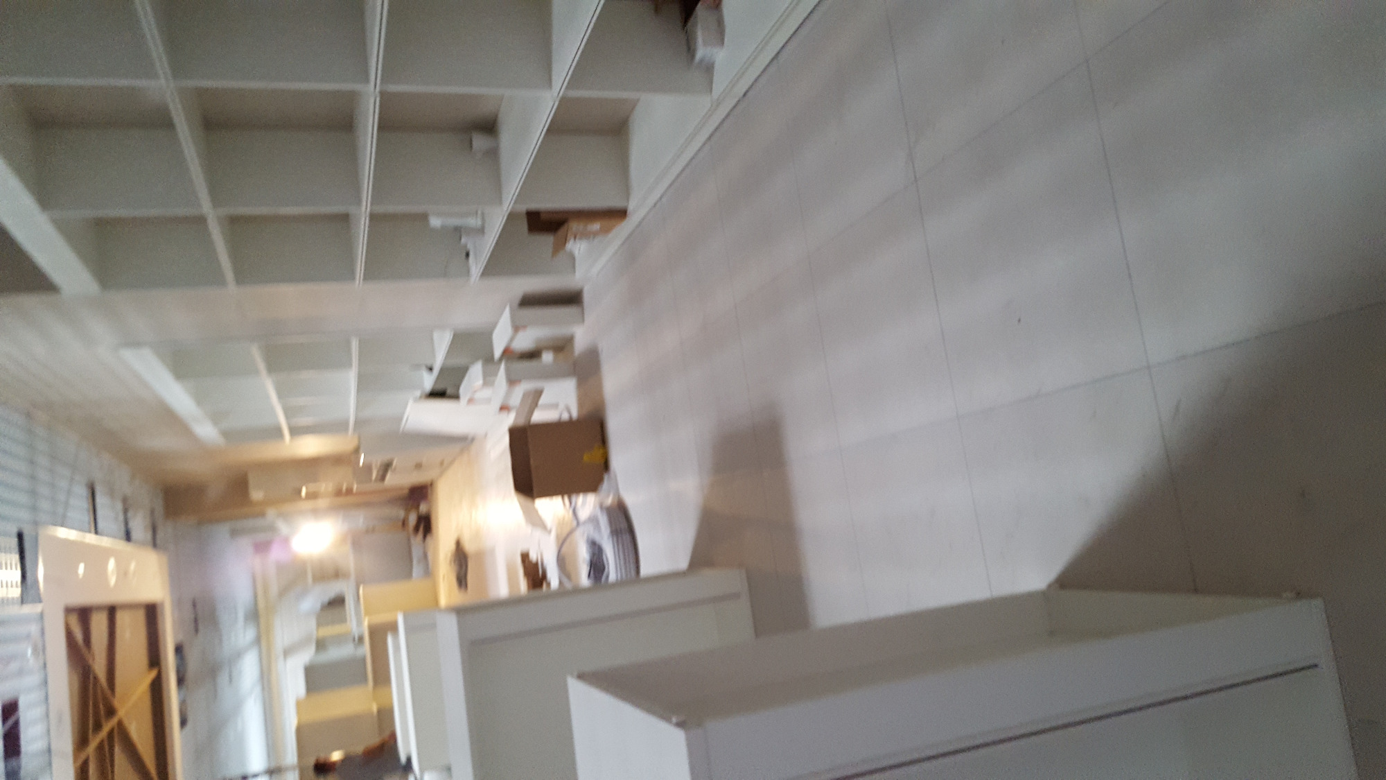 Wnętrze z białymi, częściowo zmontowanymi meblami, kartonem i widoczną konstrukcją sufitową z podziałem na kwadraty.