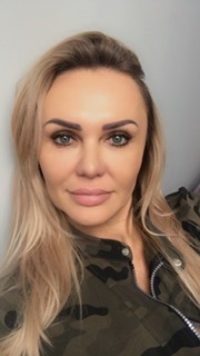 Portret kobiety z blond włosami, ubrana w kurtkę moro, z delikatnym makijażem i jasnymi oczami, skierowana w stronę obiektywu.