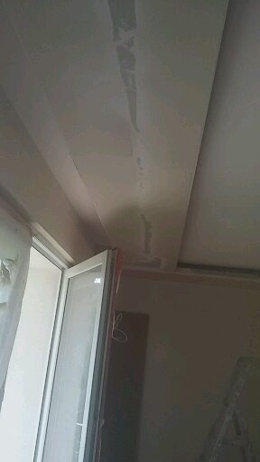 Szpachlowany sufit z widocznymi łączeniami płyt gipsowo-kartonowych, przygotowany do malowania, z otwartym oknem w tle.