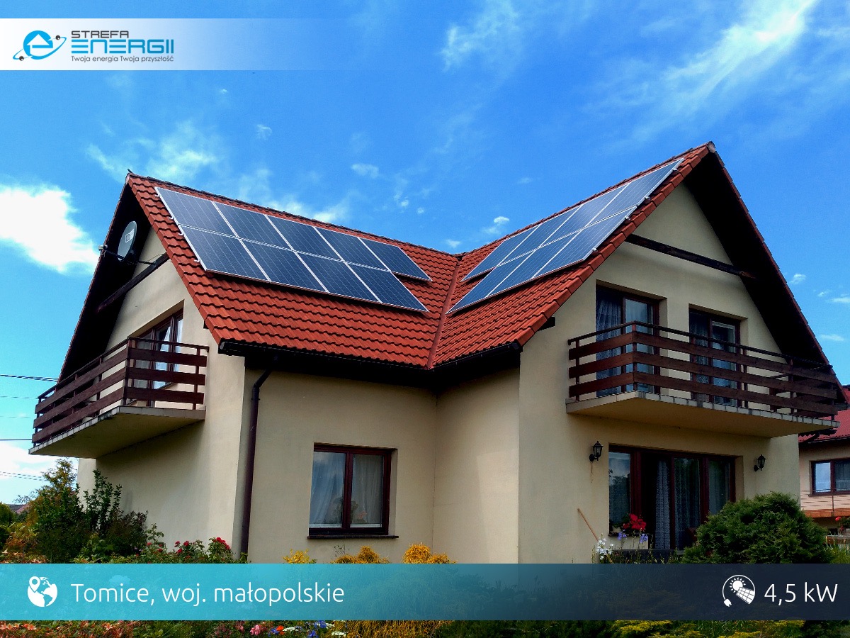 Dom jednorodzinny z czerwoną dachówką i panelami słonecznymi na dachu, widok z dołu, błękitne niebo w tle.