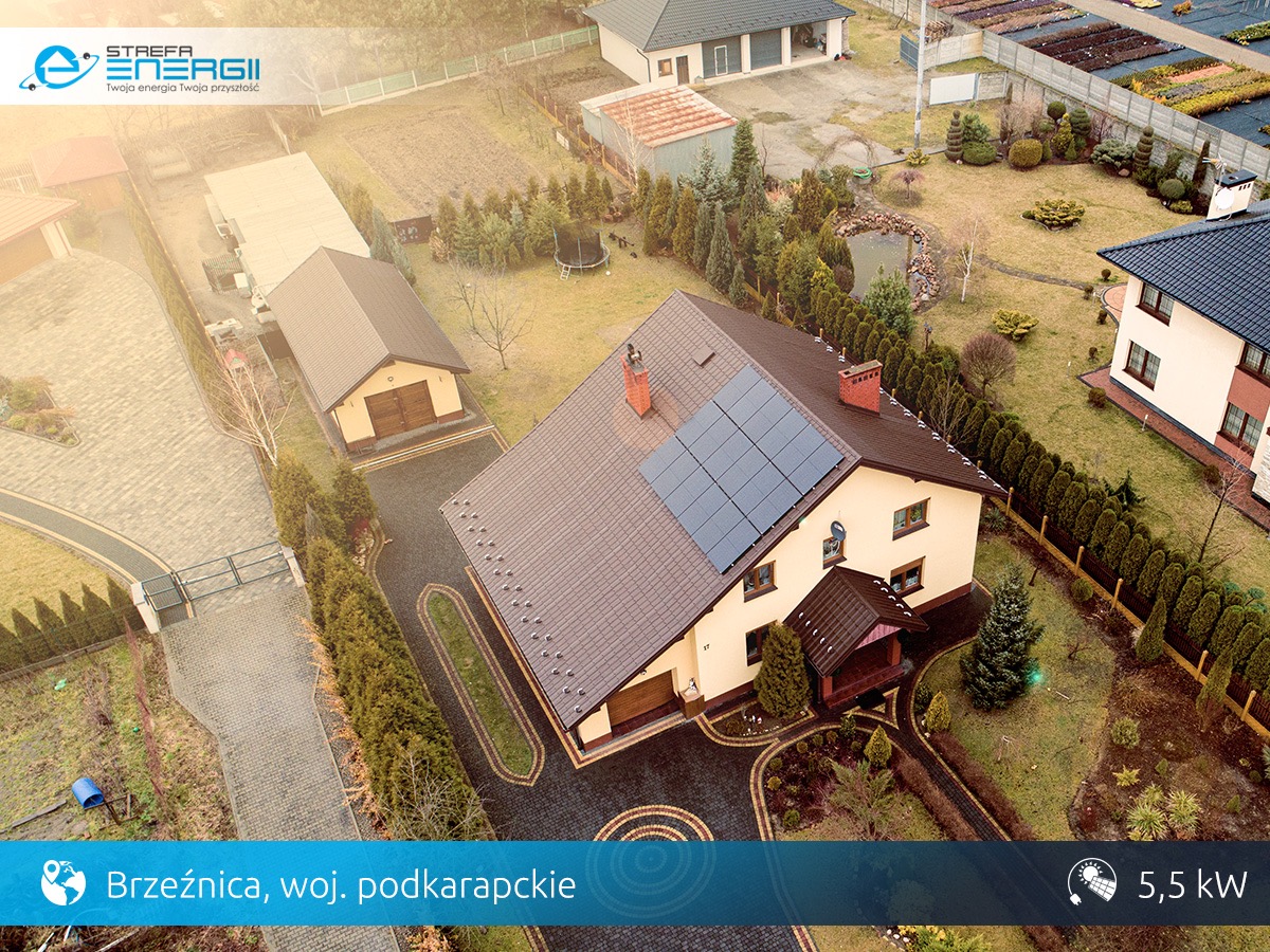 Widok z lotu ptaka na dom jednorodzinny z brązowym dachem i panelami fotowoltaicznymi na połaci, zadbany ogród, Brzeźnica, woj. podkarpackie, instalacja 5,5 kW.