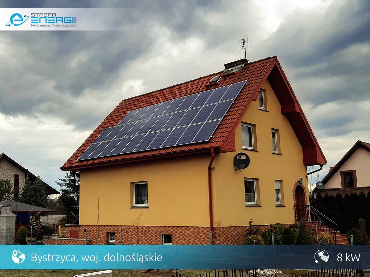 Żółty dom jednorodzinny z czerwonym dachem, na którym zamontowano panele słoneczne; widoczna antena satelitarna i logo firmy na zdjęciu w rogu.