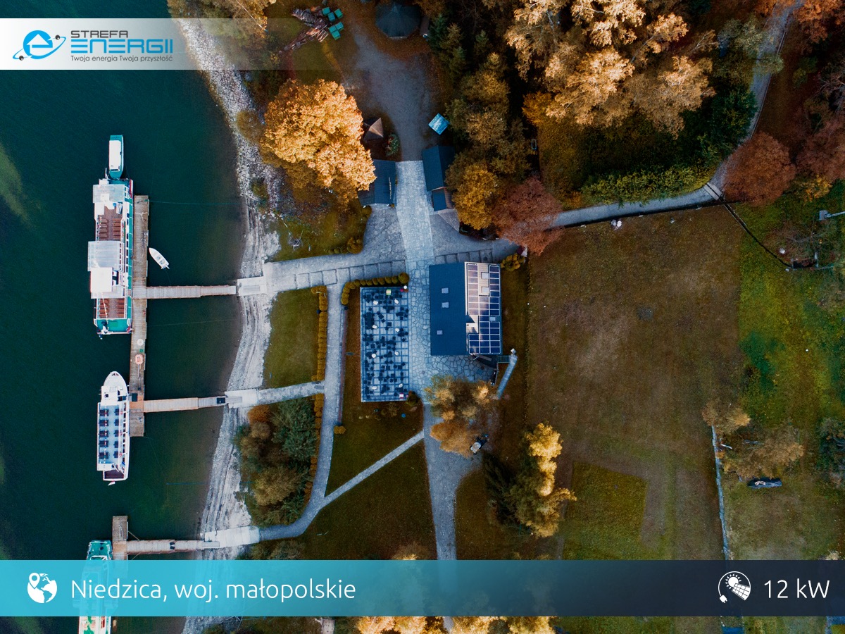 Widok z drona na budynek z panelami słonecznymi obok jeziora z przystanią i statkami w Niedzicy, Małopolska.