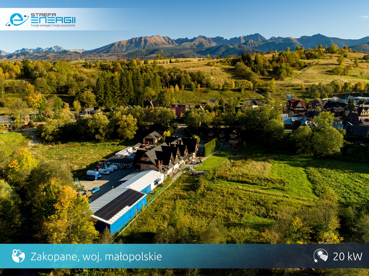 Widok z lotu ptaka na budynek z panelami słonecznymi na dachu, otoczony zielenią i zabudową, w tle panorama gór w Zakopanem.