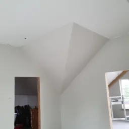 Poddasze z nietypowym skosem sufitu po wykonanych pracach, widoczne puszki z farbą i narzędzia malarskie.