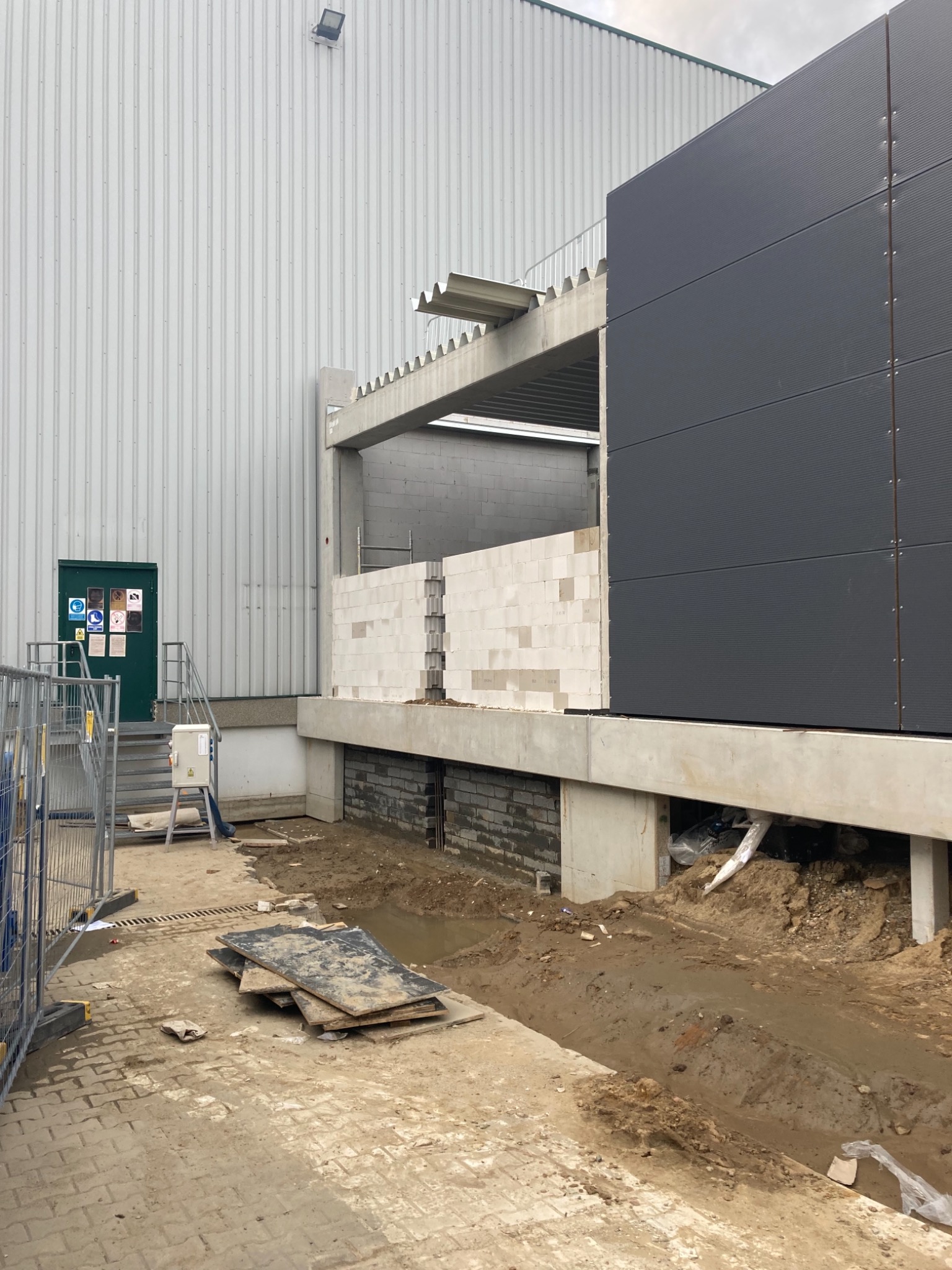 Budowa hali: fragment ściany z betonu komórkowego na fundamencie, widoczne płyty szalunkowe, konstrukcja stalowa w tle.