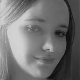 Portret kobiety z długimi włosami, uśmiechniętej, w czerni i bieli, z delikatnym oświetleniem z lewej strony twarzy.