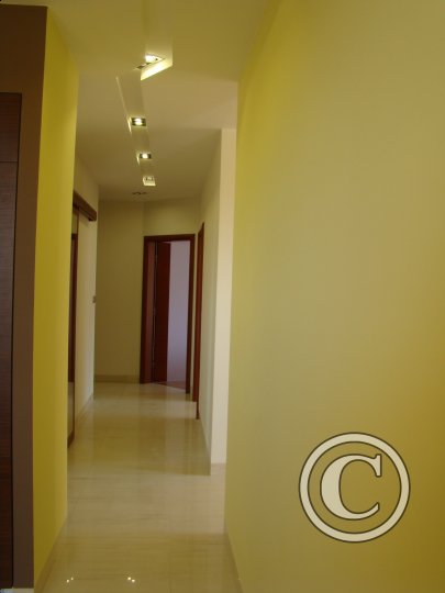 Pomalowany na żółto korytarz z błyszczącą podłogą, oświetleniem punktowym i widocznymi drzwiami, z widocznym znakiem wodnym w prawym dolnym rogu.