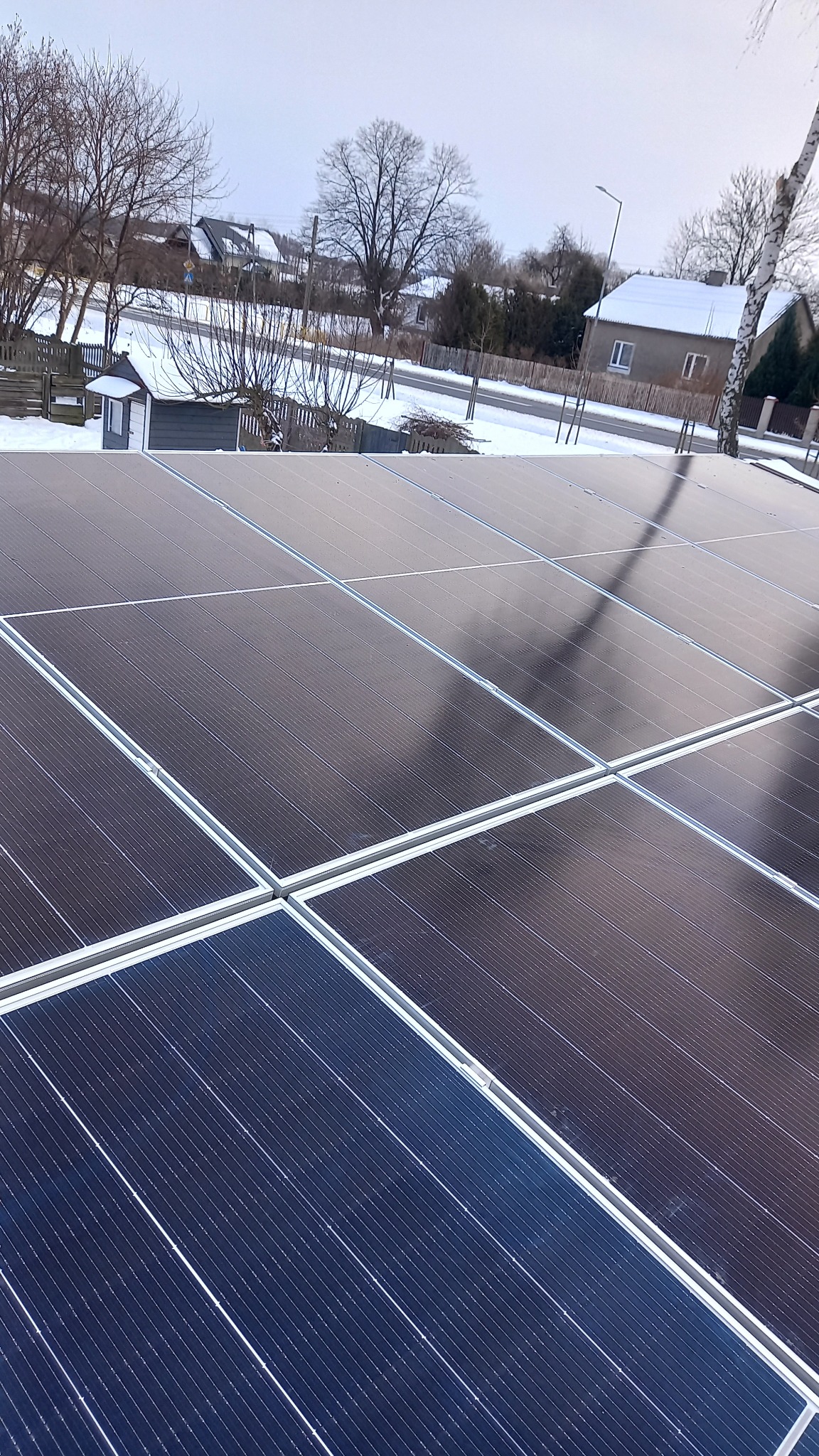 Zimowy krajobraz Krzętowa widziany z perspektywy nowo zainstalowanych paneli fotowoltaicznych na dachu, z widocznymi drzewami i ośnieżonymi domami w tle.